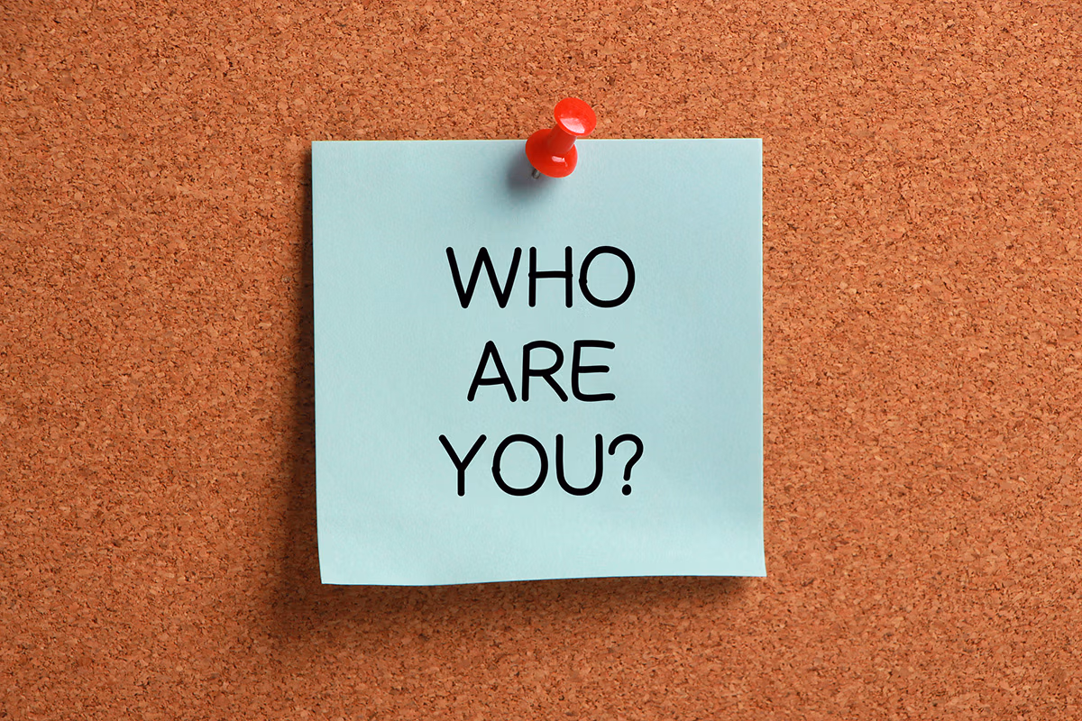 The question "Who are you" written on a light green post-it paper and pinned on a corkboard