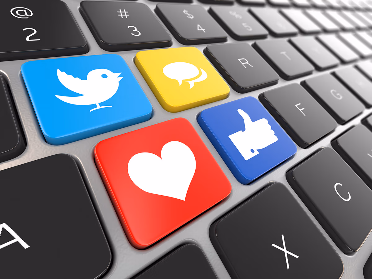 a cropped laptop keyboard image with keys replaced by social media icons - a white bird in a blue background, a white heart in red background, a white thumbs up in a dark blue background, and a white comment in yellow background