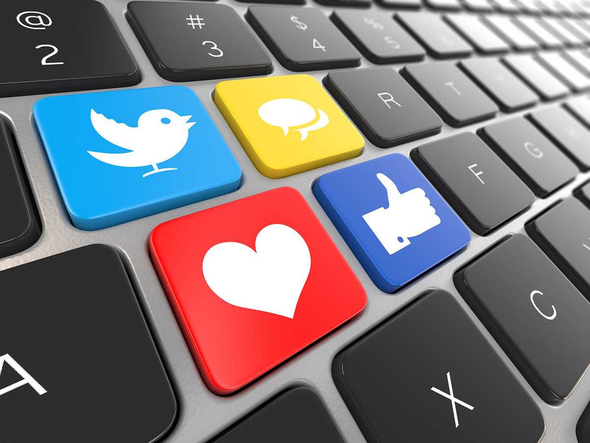 a cropped laptop keyboard image with keys replaced by social media icons - a white bird in a blue background, a white heart in red background, a white thumbs up in a dark blue background, and a white comment in yellow background