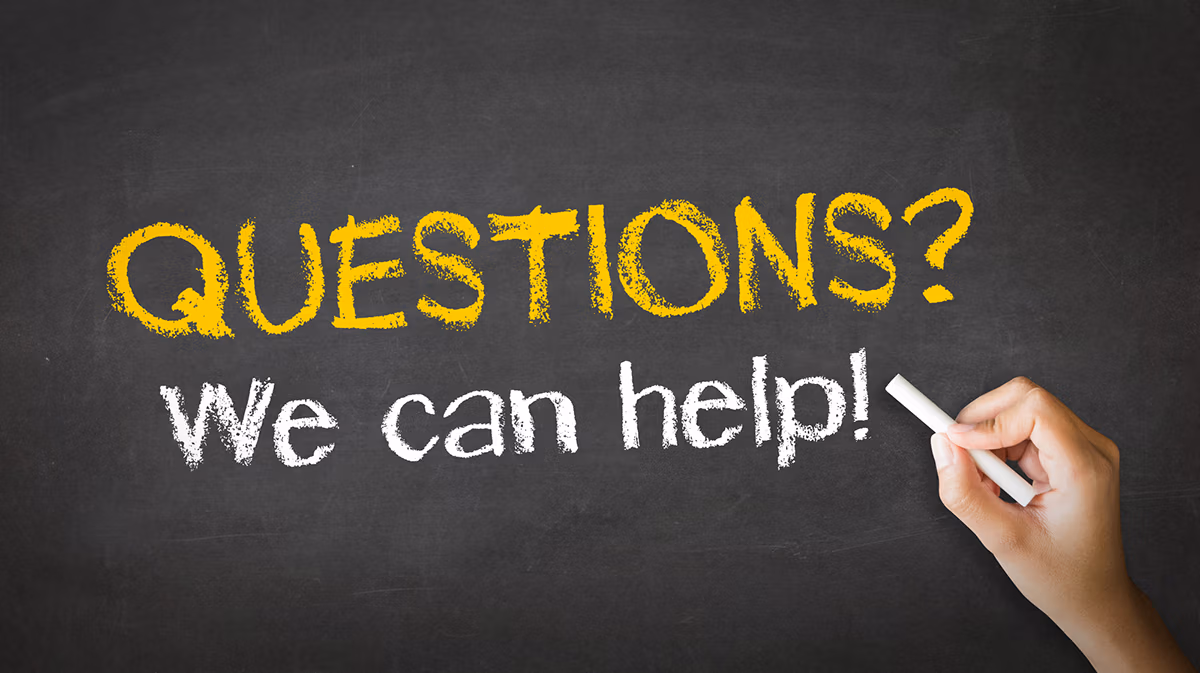 A hand holding white chalk and the sentences "Questions? We can help!" in yellow and white chalk colors on a dark gray background.