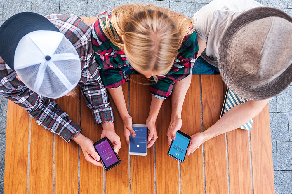 Social media activities: an overhead photo of a girl and two boys all holding and looking at their mobile phones while sitting side by side at a table