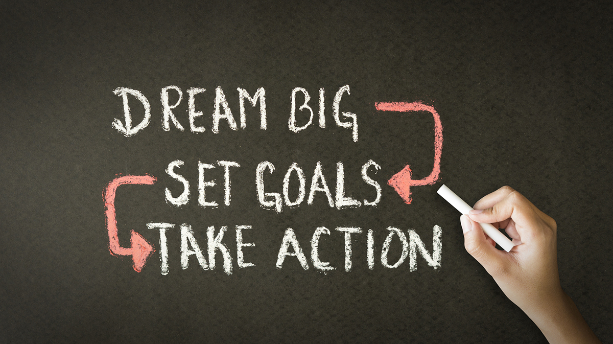 An illustration written on a gray chalkboard that reads "Dream Big - Set Goals - Take Action"